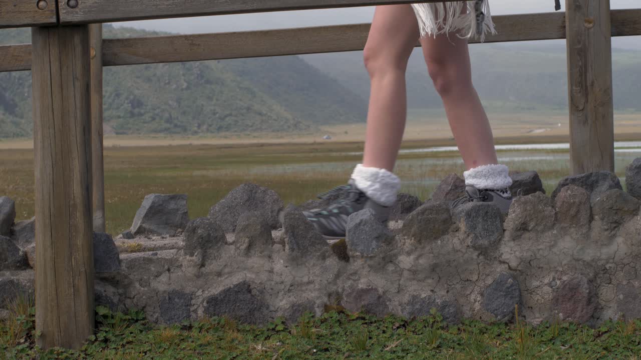 Woman walks along pathway with stone wall and wooden bridge close up on legs