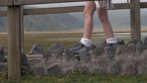 woman walks along pathway with stone wall and wooden bridge close up on legs