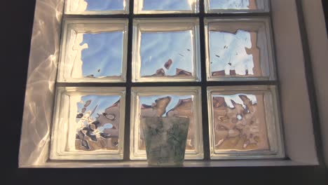 a slow moving, symmetrical shot of a window with a glass pot on its ledge