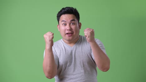 young handsome overweight asian man against green background