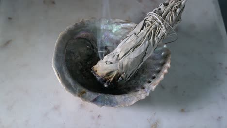 Burning-sage-in-a-shell-on-a-wood-table-with-black-background-showing-sage-smoke