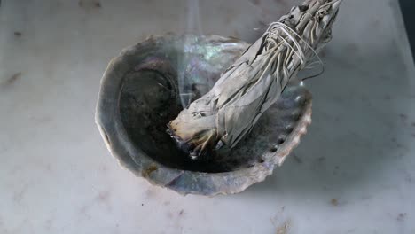 salvia ardiente en una concha sobre una mesa de madera con fondo negro que muestra humo de salvia