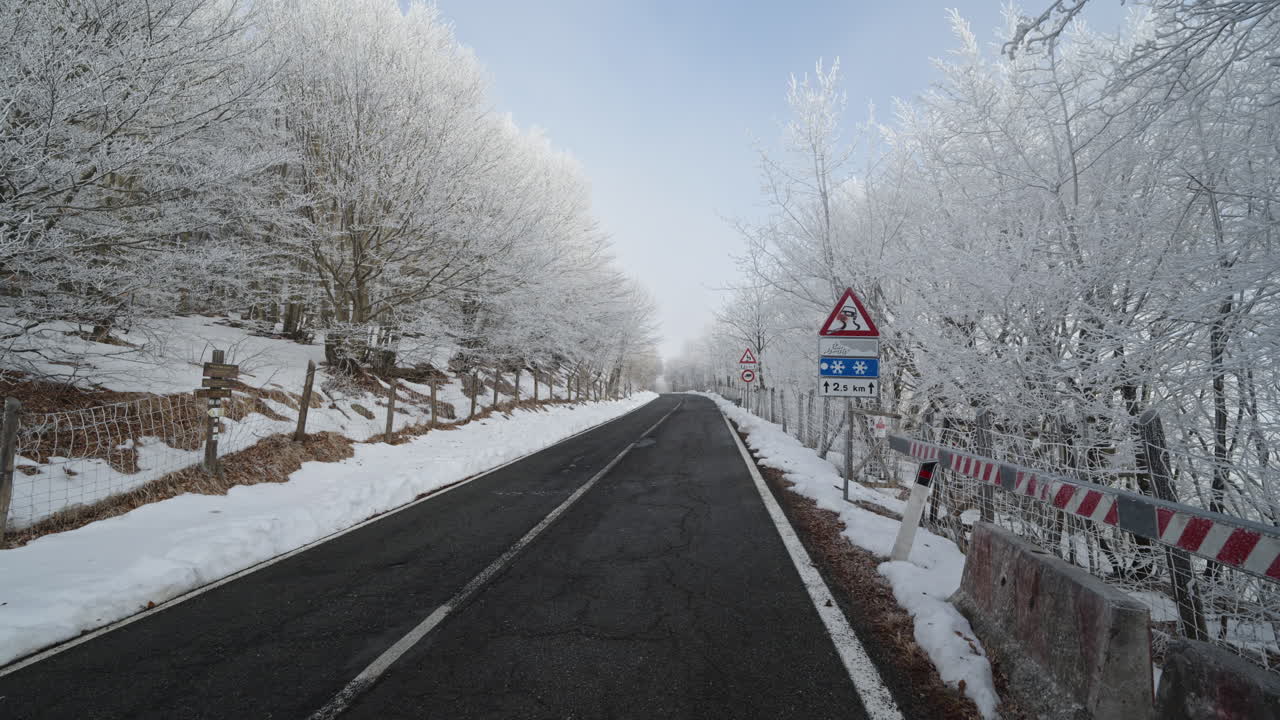 Snowy winter road, trees covered in frost, warning signs for icy conditions ahead
