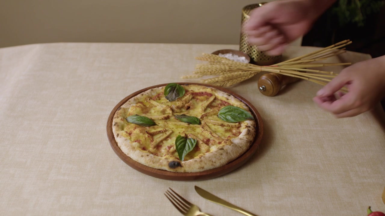 Hands arranging a fresh baked flatbread with basil on a decorated dining table