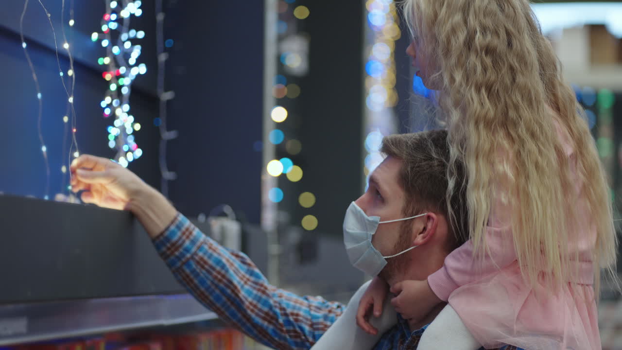 papá e hija eligen adornos y guirnaldas con juguetes para árboles de navidad y en casa en la tienda. guirnaldas navideñas y decoración