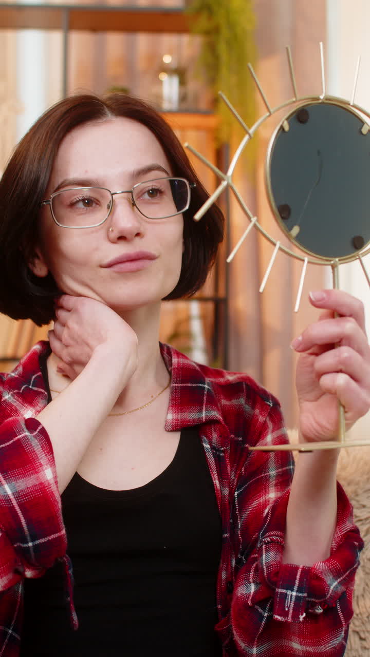Mulher jovem tentando novos óculos no espelho sorrindo enquanto verifica o reflexo com satisfação