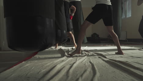 hombres hacen ejercicios en grupo con bolsas de boxeo en un gimnasio público de cerca. fuertes kickboxers trabajan en la técnica durante el entrenamiento en la alfombra en el club de lucha en cámara lenta