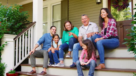 la familia de varias generaciones se sienta en los escalones que conducen al porche de la casa