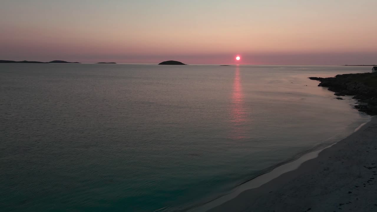 Reverse drone shot of Scottish sunset with beach and blue water in foreground
