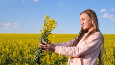 happy young woman admiring enjoying a yellow bouquet of rapeseed happy young woman admiring enjoying a yellow bouquet of rapeseed girl on the background of a field of canola and blue sky