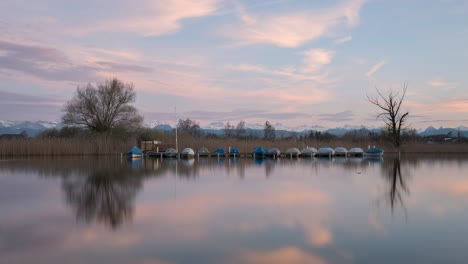 calm sunset on a lake with snowy mountains in the background and boats on the water