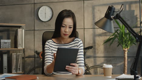 Young-Pretty-And-Smiled-Woman,-Office-Worker,-Tapping-And-Scrolling-On-The-Tablet-Device-In-Her-Hands-At-The-Working-Table