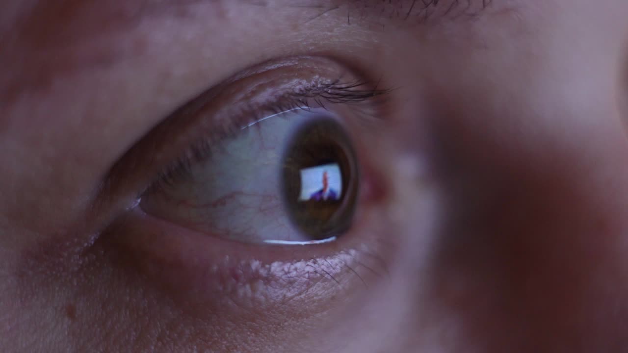 Reflection in the eyes of light from the screen. Fast running news feed. A huge amount of information for a person through the media. MACRO. Eyeball surface reflecting the image seen on a monitor. Strained eyes