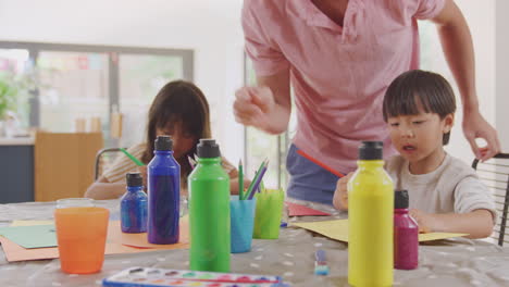 asian father having fun with children doing craft on table at home