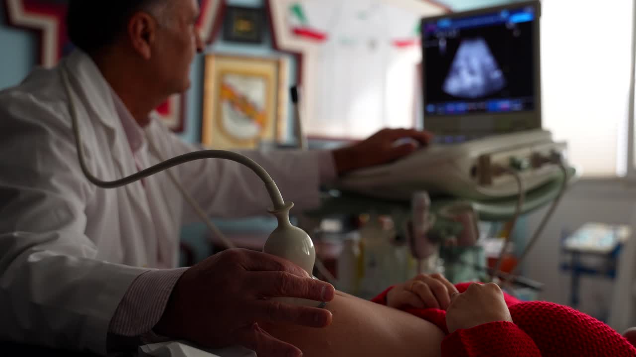 Un medico esegue un esame ecografico, concentrandosi sul ventre di una donna incinta e sulle immagini dello schermo.