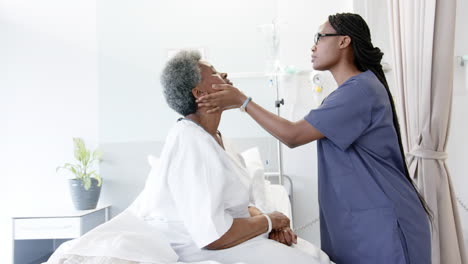 african american female doctor testing eyes of senior female patient in hospital room, slow motion