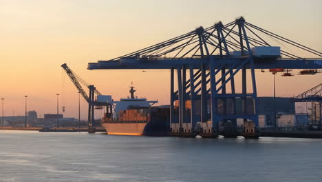 container ship docked at port during golden hour with gantry crane