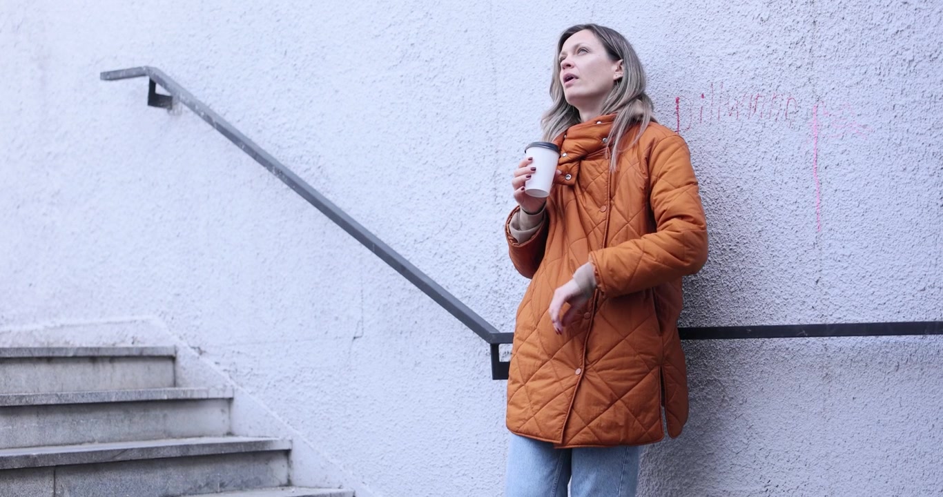 Donna beve caffè guardando l'orologio da polso con delusione.