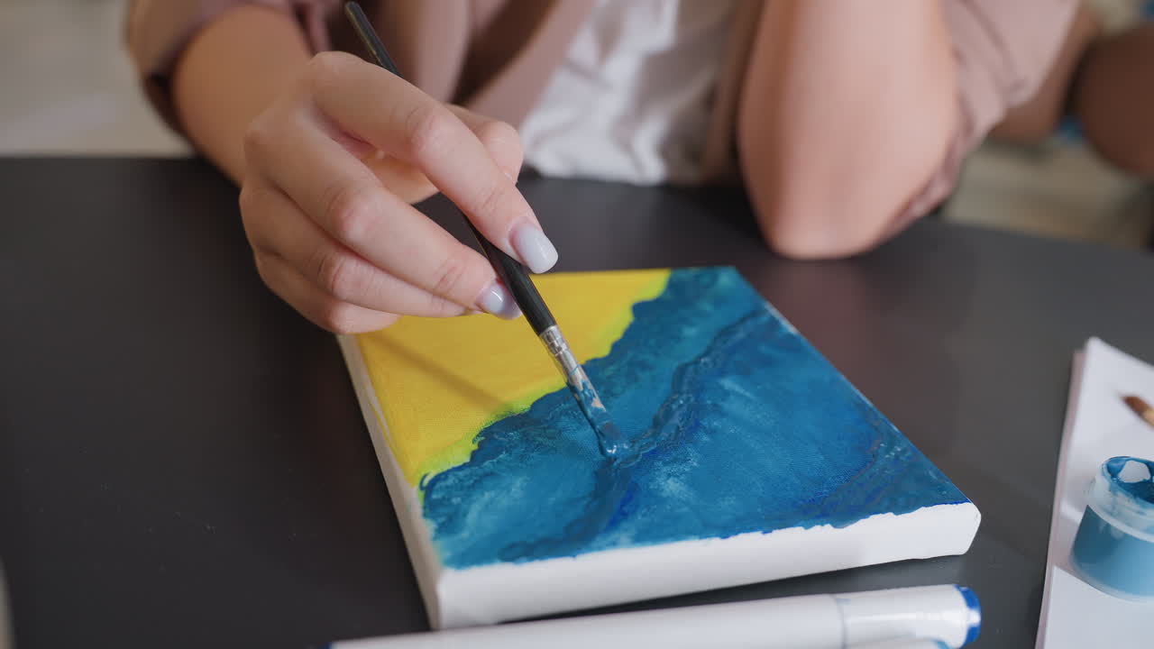 ilustración con olas texturizadas, escena de estudio reflectante que captura el proceso detallado de pintura marina, primer plano de un artista aplicando tonos azules en capas sobre un fondo amarillo en un espacio de trabajo compacto