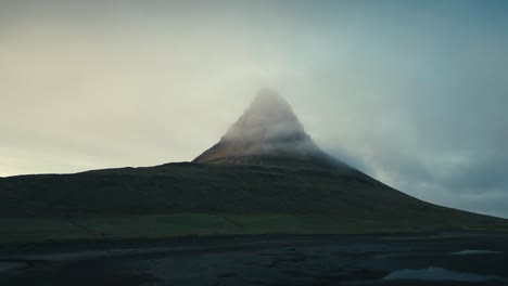 Wunderschöne-Drohnenluftaufnahme-Eines-Einzelnen-Grünen-Berggipfels-Mit-Nebliger-Wolkendecke