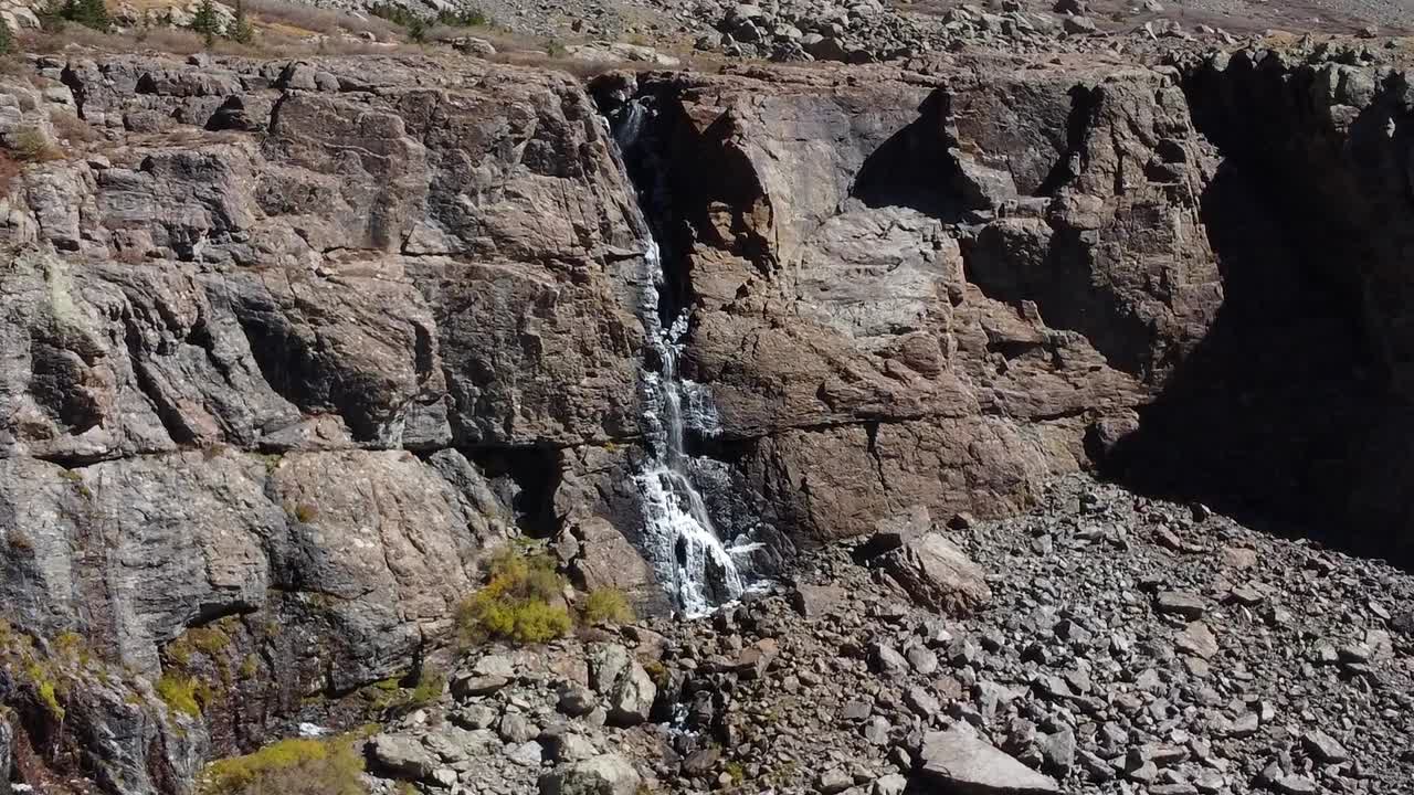 volando a través de los árboles sobre el lago de montaña colorado hacia la cascada de deshielo del lago willow, antena