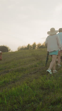 familia tomando un paseo pacífico en una colina cubierta de hierba con su perro al atardecer, disfrutando de la naturaleza, una joven lleva una canasta de mimbre mientras otros caminan delante