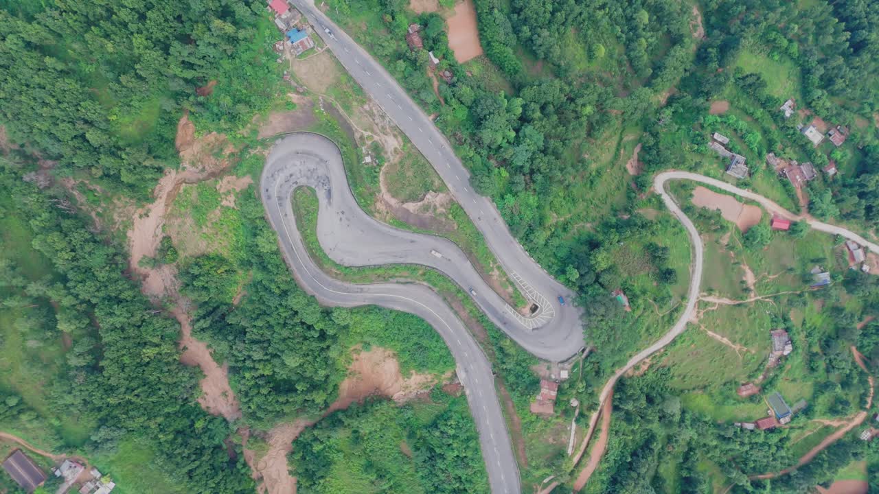 Aerial view of a vehicle driving along a winding hillside road surrounded by lush green mountains, showcasing scenic mountain travel, nature, and rural transportation beauty