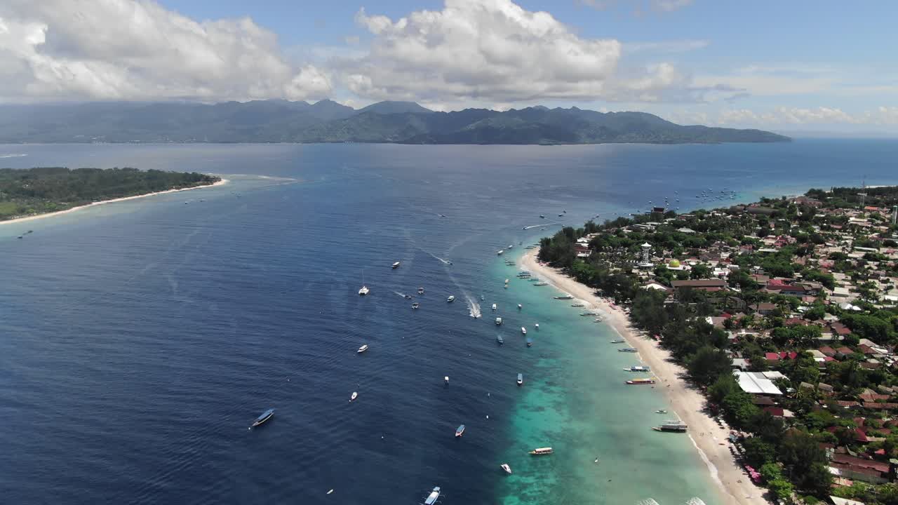 Boats cruising through the turquoise coastline waters off of sunny Gili Trawangan island. Aerial