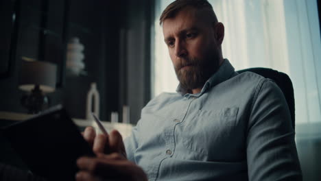 thoughtful financial analyst working on tablet computer with digital stylus, monitoring real-time stocks, exchange market charts. successful businessman works in comfortable office of investment bank.