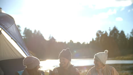 Mother,-daughter-and-grandmother-talk-outside-tent-by-a-lake