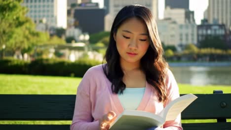 a young woman sits comfortably on a park bench, absorbed in a book as sunlight dances on the pages. the city skyline provides a stunning backdrop while nature surrounds her.