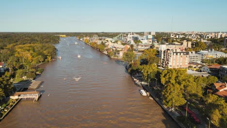 Aerial-dolly-in-of-Tigre-rowing-club-and-amusement-park-beside-de-la-Plata-River-surrounded-by-trees-at-sunset,-Buenos-Aires