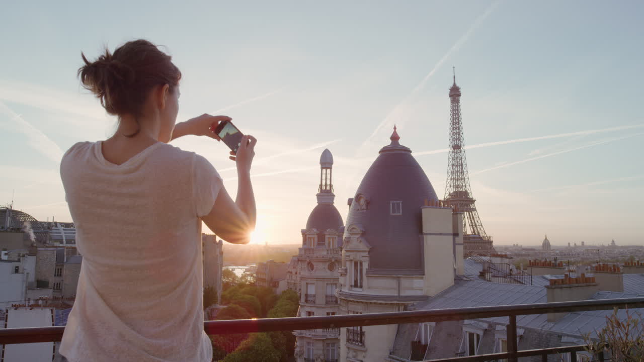 happy woman using smartphone taking photo enjoying sharing summer vacation experience in paris photographing beautiful sunset view of eiffel tower on balcony