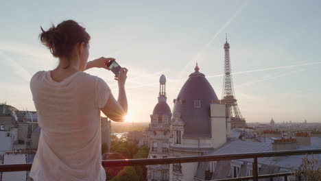 Glückliche-Frau,-Die-Ihr-Smartphone-Nutzt,-Um-Ein-Foto-Zu-Machen-Und-Es-Zu-Genießen,-Ihre-Sommerurlaubserfahrung-In-Paris-Zu-Teilen-Und-Die-Wunderschöne-Aussicht-Auf-Den-Sonnenuntergang-Des-Eiffelturms-Auf-Dem-Balkon-Zu-Fotografieren