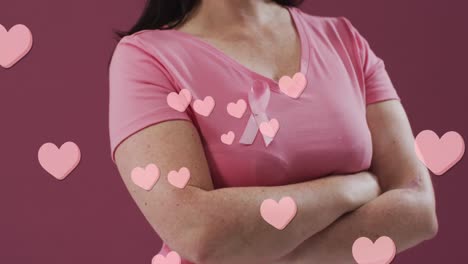 animation of hearts text over caucasian woman with pink ribbon on pink background