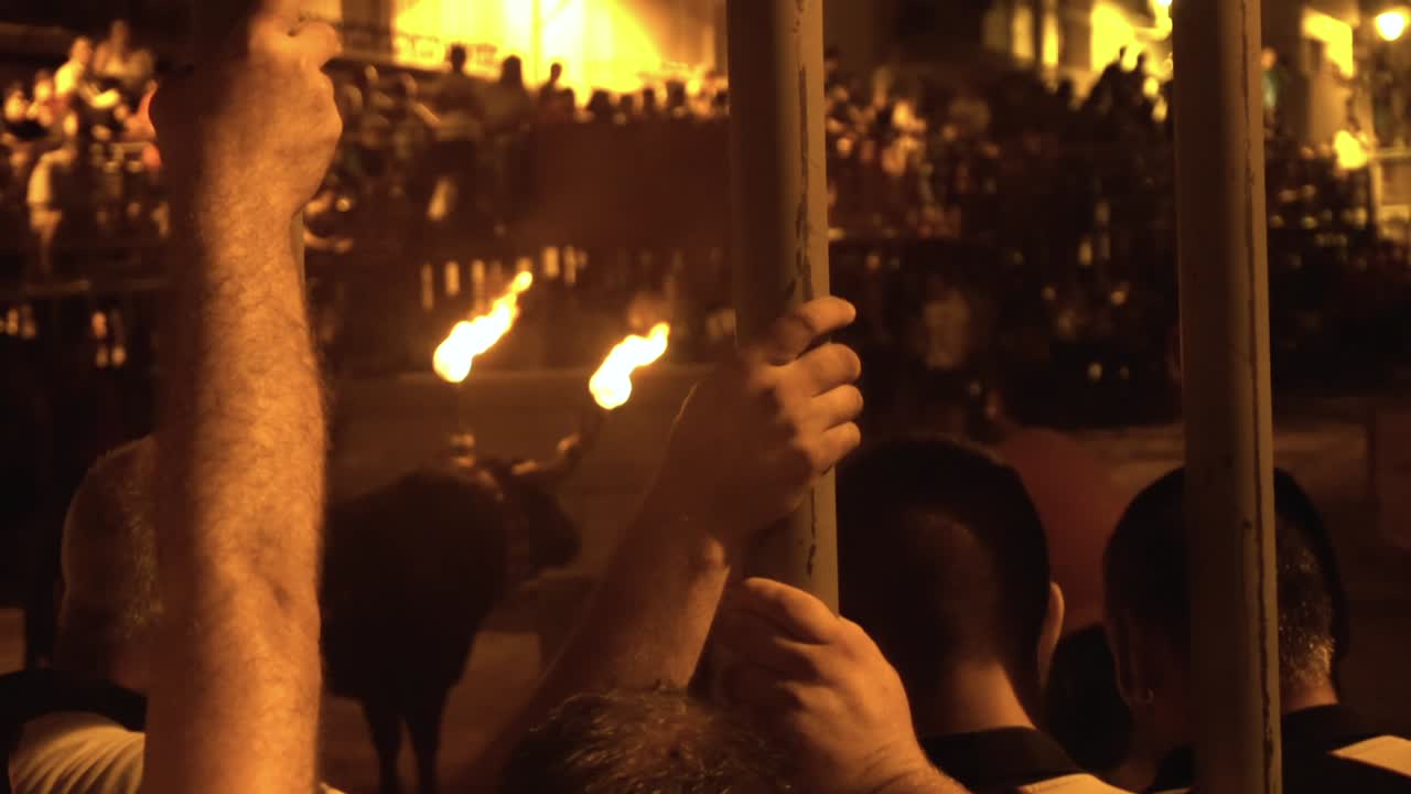 Spanish People Watching Annual Bull Fight Event In Calig, Valencia, Spain At Night With Fire On Bull's Horns - medium shot