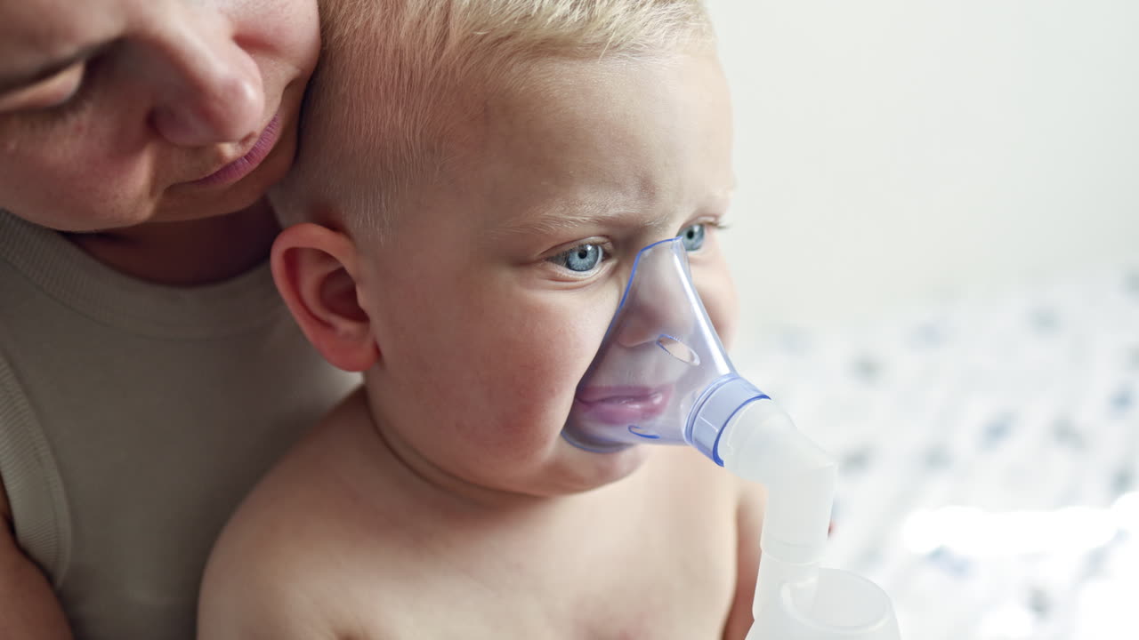 Therapeutic inhalation with a mask on the child's face. The child breathes through a nebulizer with cough medicine. Treatment of the child at home. Inhalation of the child at home