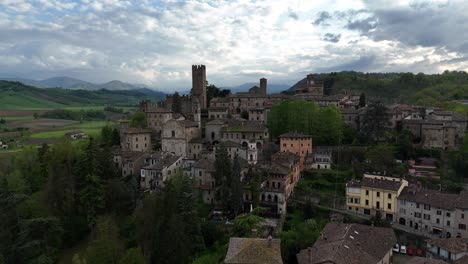 Drone view of Castell'Arquato medieval skyline showing Visconti Castle, clock tower and stone houses, surrounded by hills and woods, overcast spring sky