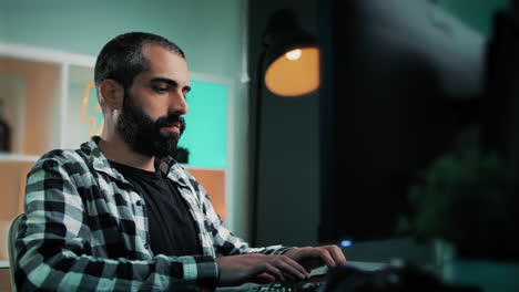 Handsome-Caucasian-employee-or-freelancer-working-from-home-sitting-behind-a-desk-developing-a-project-at-his-cool-office-with-a-lightning-bolt-neon-sign-and-teal-and-orange-lights-in-the-background