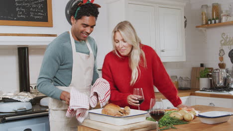 hombre sacando el pavo del horno como pareja bebiendo vino y preparando la cena el día de navidad