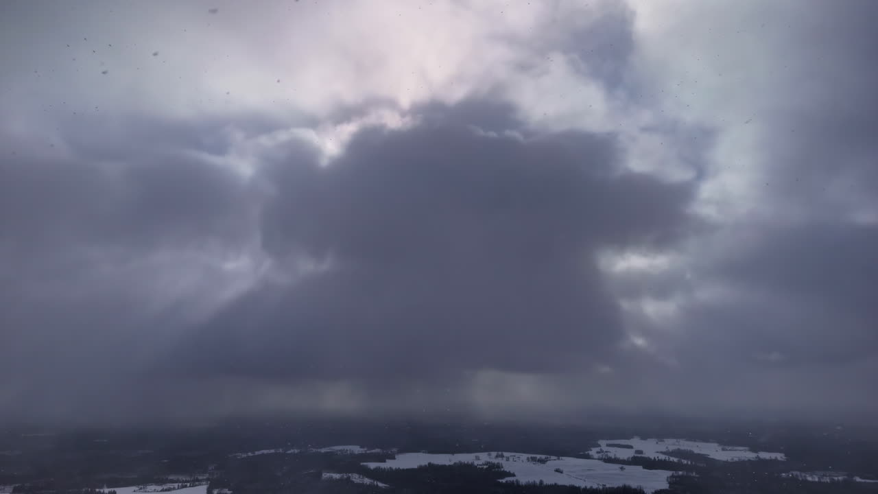 Dark storm clouds gathering over sky, soft light breaking through moody atmosphere, aerial snowing static backdrop