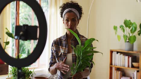 Mixed-race-female-vlogger-transplanting-plants-in-pot-and-recording-on-smartphone-at-home