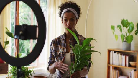 vlogger de raza mixta trasplantando plantas en maceta y grabando en el teléfono inteligente en casa