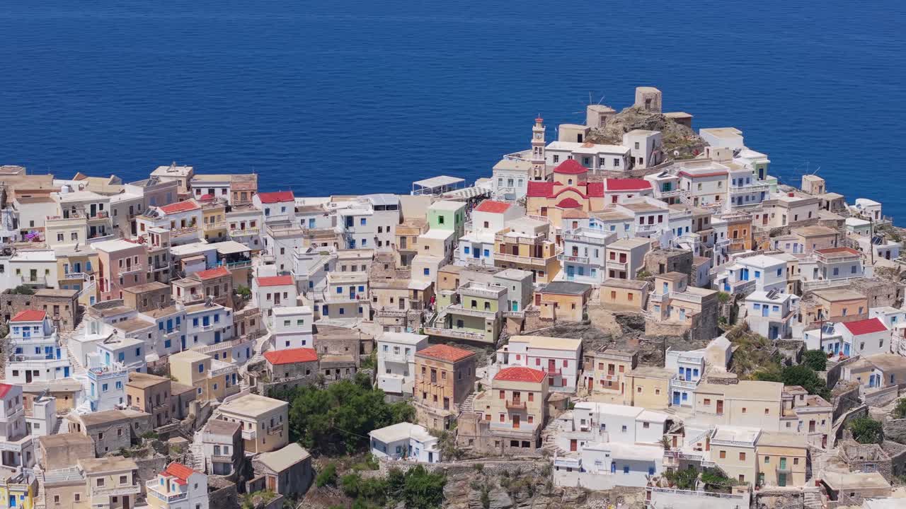 Lateral and high-angle drone movement captures the colorful houses of Olympos village at the mountain peak in Karpathos, showcasing traditional architecture and scenic Aegean surroundings