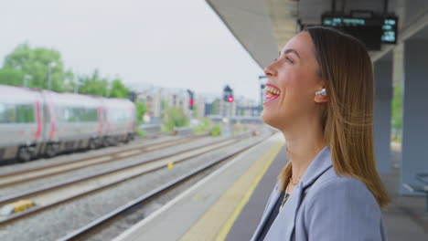 businesswoman waiting on train platform with wireless earbuds answers call on mobile phone