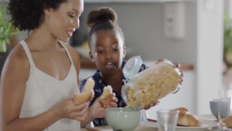 happy african american mother and daughter eating breakfast in kitchen, slow motion