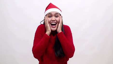 wow excitada mujer asiática con un suéter rojo cálido y sombrero de navidad está mirando a la cámara mientras abre la boca de pie aislado en fondo blanco