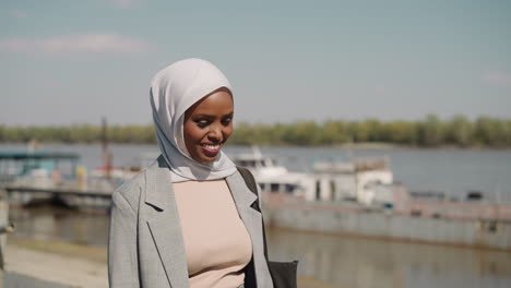 smiling arabic woman with hijab walks along embankment