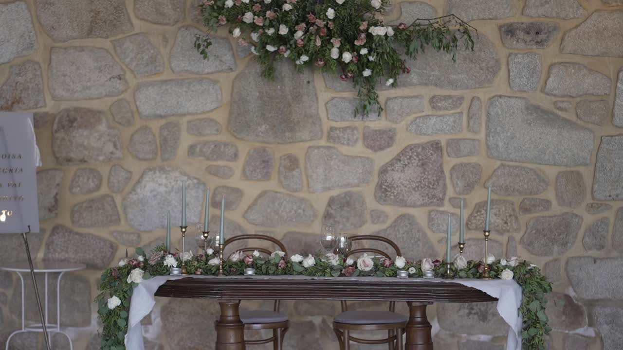 Romantic wedding sweetheart table with floral arrangements, set against a rustic stone wall