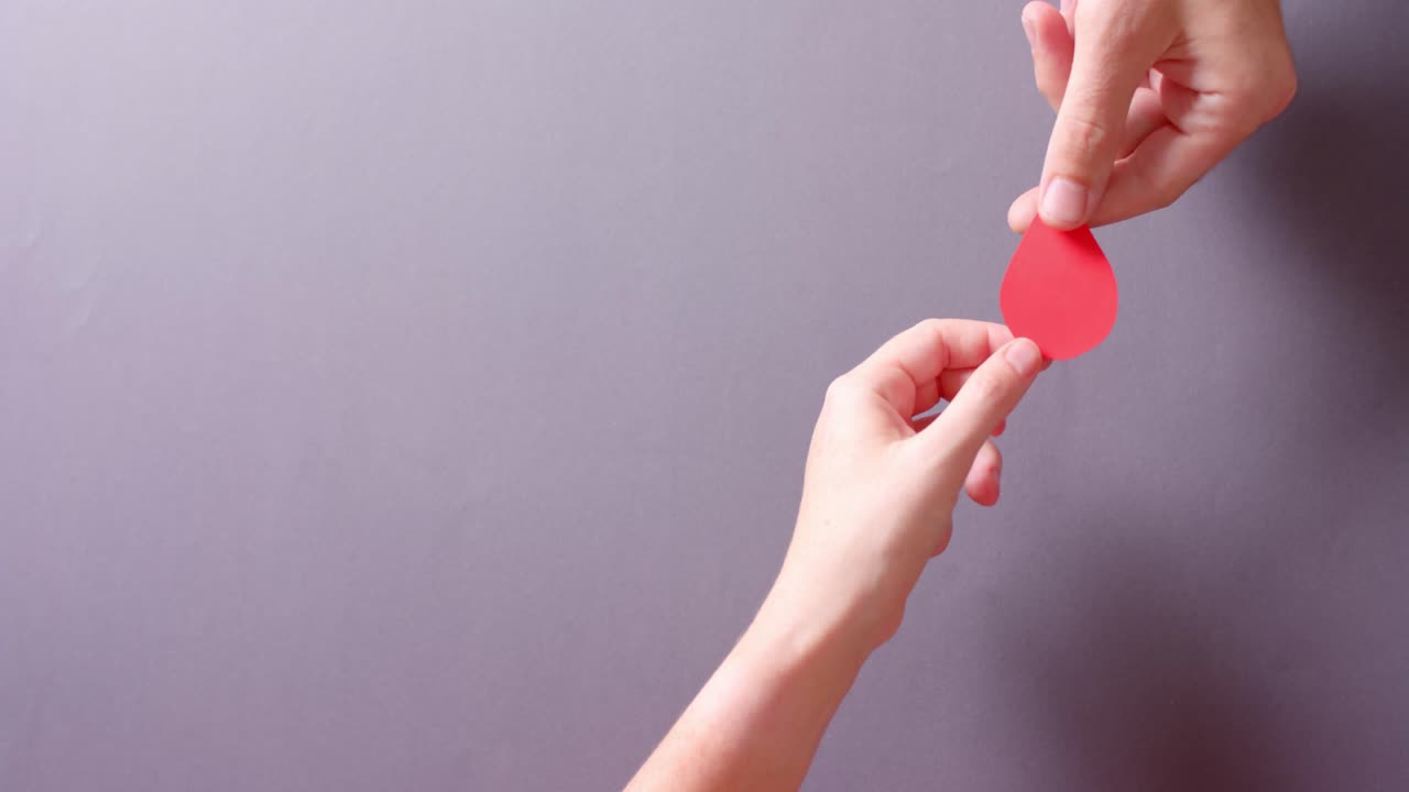 manos de personas caucásicas dando gota de sangre en fondo gris con espacio de copia, cámara lenta